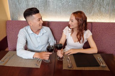 Gülümseyen genç erkek arkadaş ve kız arkadaş ilk yıl dönümünü kutlarken birbirlerine bakarlar.