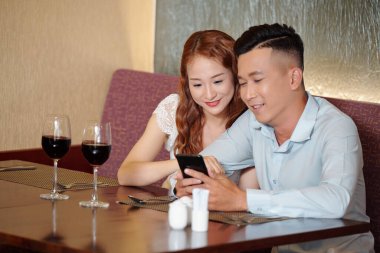 Kafe masasında oturup şarap içen ve sosyal medyada ilginç şeyler okuyan ya da ünlü blogcuların yeni videolarını izleyen mutlu genç bir çift.