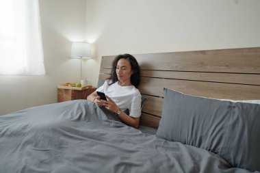 Siyah uzun saçlı yakışıklı Vietnamlı adam, lambası değişmiş ve sabah vaktini boşa harcarken telefonunu kullanıyor.