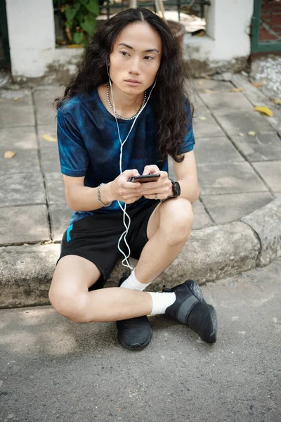 Серьезный Красивый Молодой Азиат Вьющимися Волосами Сидит Обочине Слушает Аудиосообщение — стоковое фото