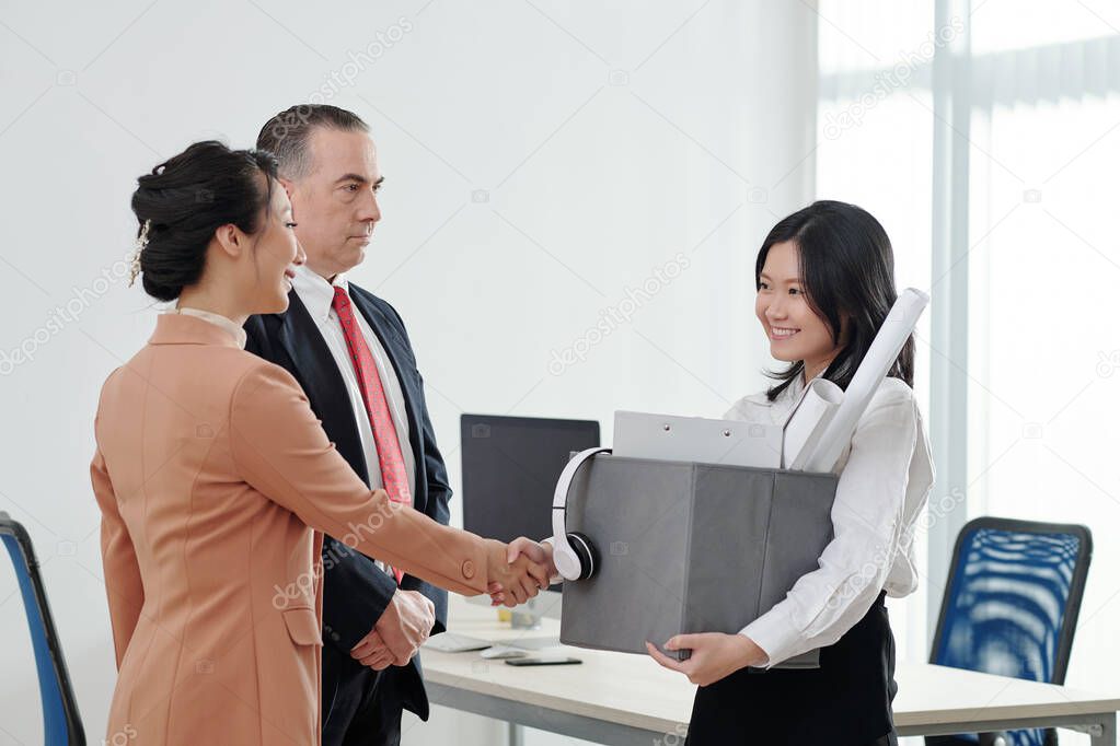 Businesswoman with box of belongings shaking hands of her new colleagues