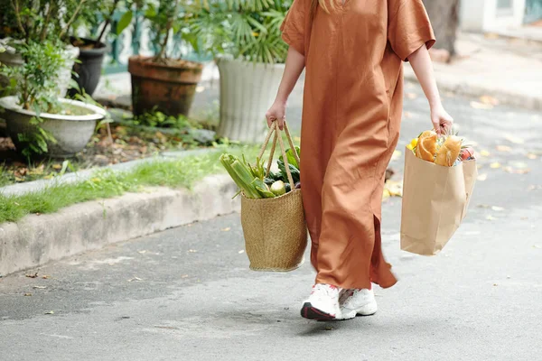 長いリネンのドレスと新鮮な食料品と重い袋を運ぶスニーカーの女性 — ストック写真