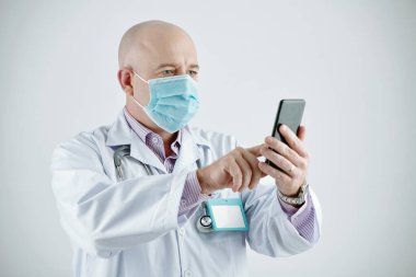 Cep telefonu kullanan maskeli bir doktor.