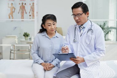 Doktor kıdemli hastayla konuşuyor, sorular soruyor ve aile geçmişi hakkında bilgi yazıyor.