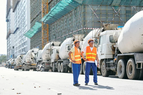 Robotnicy budowlani stojący przy zaparkowanych samochodach ciężarowych — Zdjęcie stockowe