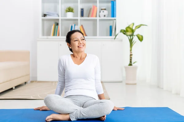 Yoga mat üzerinde oturan Olgun kadın — Stok fotoğraf