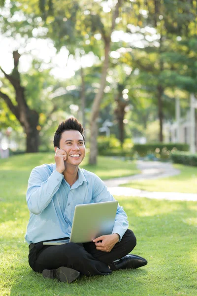 Biznesmen w parku z laptopa i rozmowy na telefon — Zdjęcie stockowe