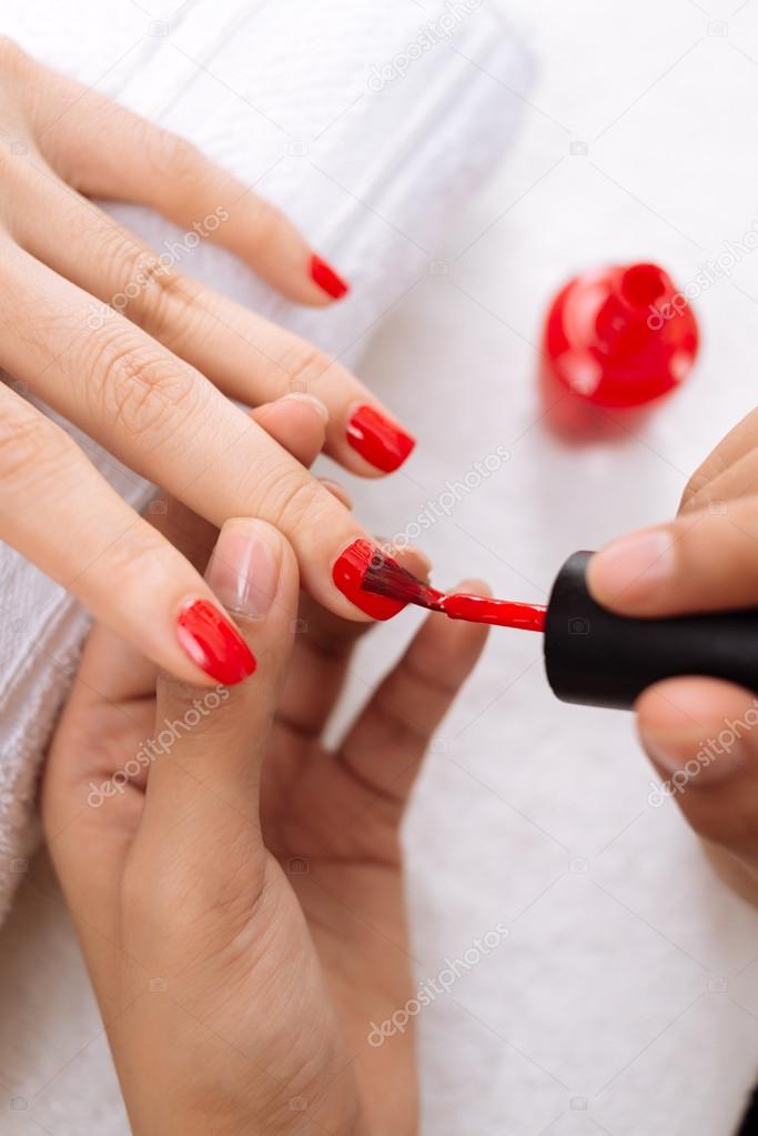 Applying red nail polish to finger nails