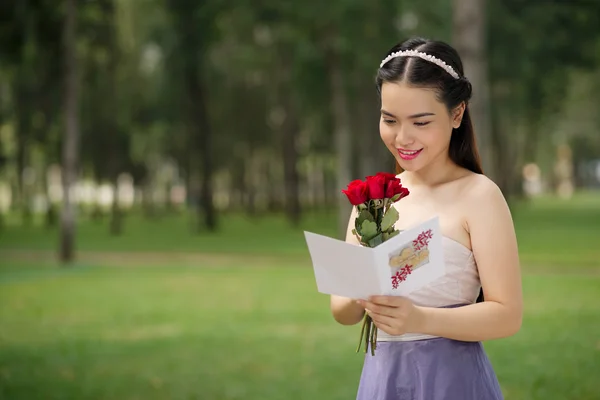 Ragazza con fiori che legge un biglietto di auguri — Foto Stock