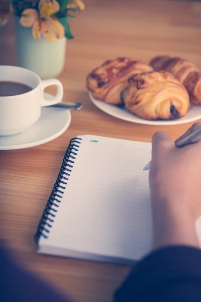 Person writing with coffee and pastries — Stock Photo, Image