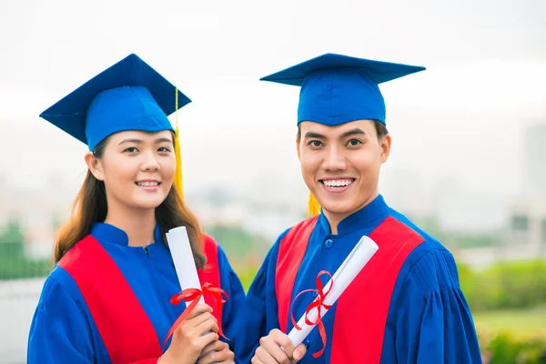 Graduates in gowns holding diplomas — Stock Photo, Image