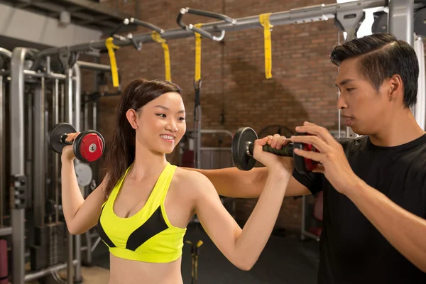 Woman picking up dumbbells with instructor — Stock Photo, Image