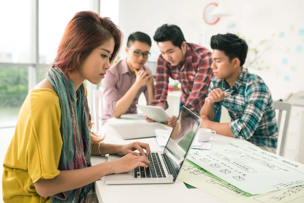 Girl working on laptop while her colleagues talking — Stock Photo, Image