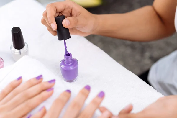 Маникюрша наносит фиолетовый лак для ногтей — стоковое фото