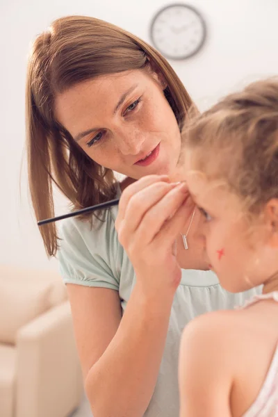 Woman painting face of her daughte — Stock Photo, Image