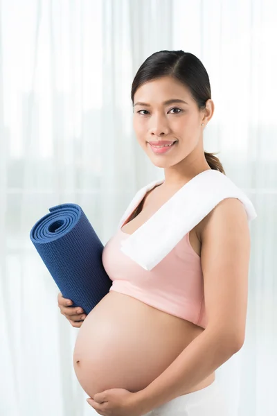 Беременная женщина с ковриком для упражнений — стоковое фото