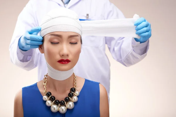 Médico removendo ligaduras da cabeça da mulher — Fotografia de Stock