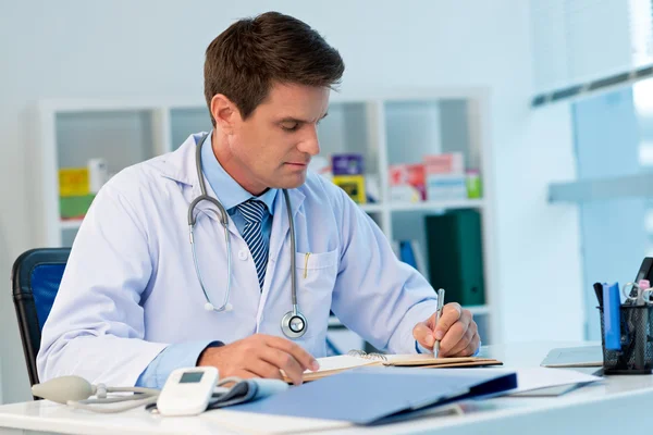 Médico geral escrevendo em caderno — Fotografia de Stock