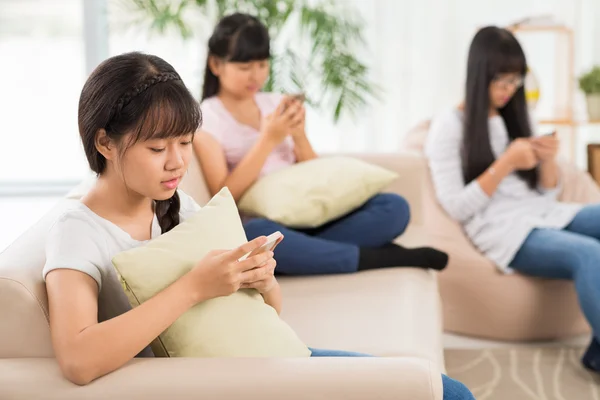 Mädchen und ihre Freunde sitzen und SMS schreiben — Stockfoto