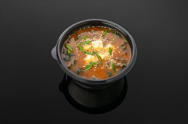 Tofu peynirli kimchi çorbası, yosun, kimchi sosu, handashi, yeşil soğan, yumurta, susam. Yukarıdan bak. Koyu ayna arkaplanı.