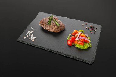 Biftek ve sebze salatası. Siyah bir tahta üzerinde. Karanlık arka plan. İzole edilmiş. Yakın plan..