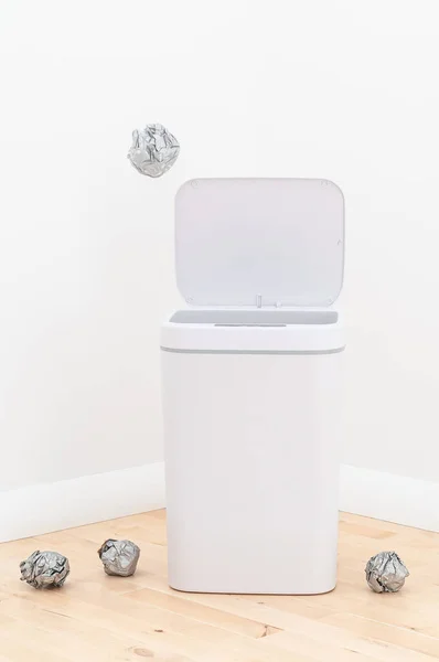 Smart waste basket. Electronic gadget for the home. The cover is open. Rubbish flies into the basket .. On the wooden floor. The background is white.