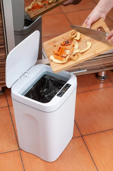 Smart waste basket. Electronic gadget for the home. Open cover. Female hands throw out trash. View from above. On brown tiles.