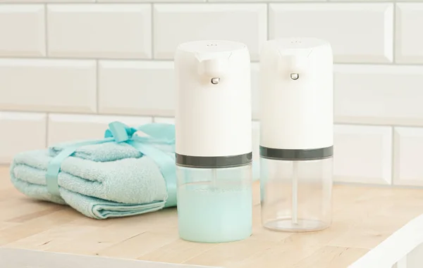 Two automatic soap dispenser. One with soap, the other is empty .. On the background is a blue towel. Close-up. Light background.