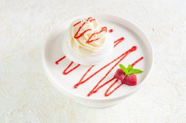 Dessert Pavlova with whipped cream. Decorated with strawberry topping, strawberries and mint. On a white plate. View from above. Light background.