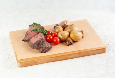 Fırında patates ve mantarlı dana biftek. Bitkiler ve vişneli domateslerle süslenmiş. Tahta bir tahtanın üzerinde servis edilmiş. Yakın plan..