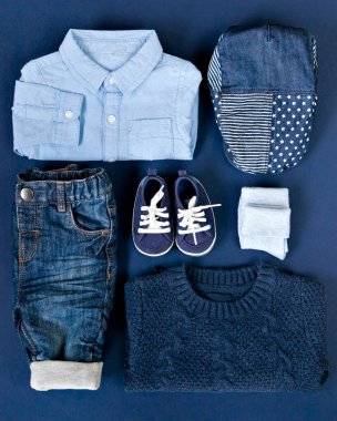 Klasik mavi arka planda sonbahar çocuğu kot giysisi. Little Boy Fashion, kış sonbahar koleksiyonu. Mavi çocuk süveteri, gömleği, pantolonu, şapkası ve botları düz bir şekilde dizilmiş. Sonbahar arkaplanı.