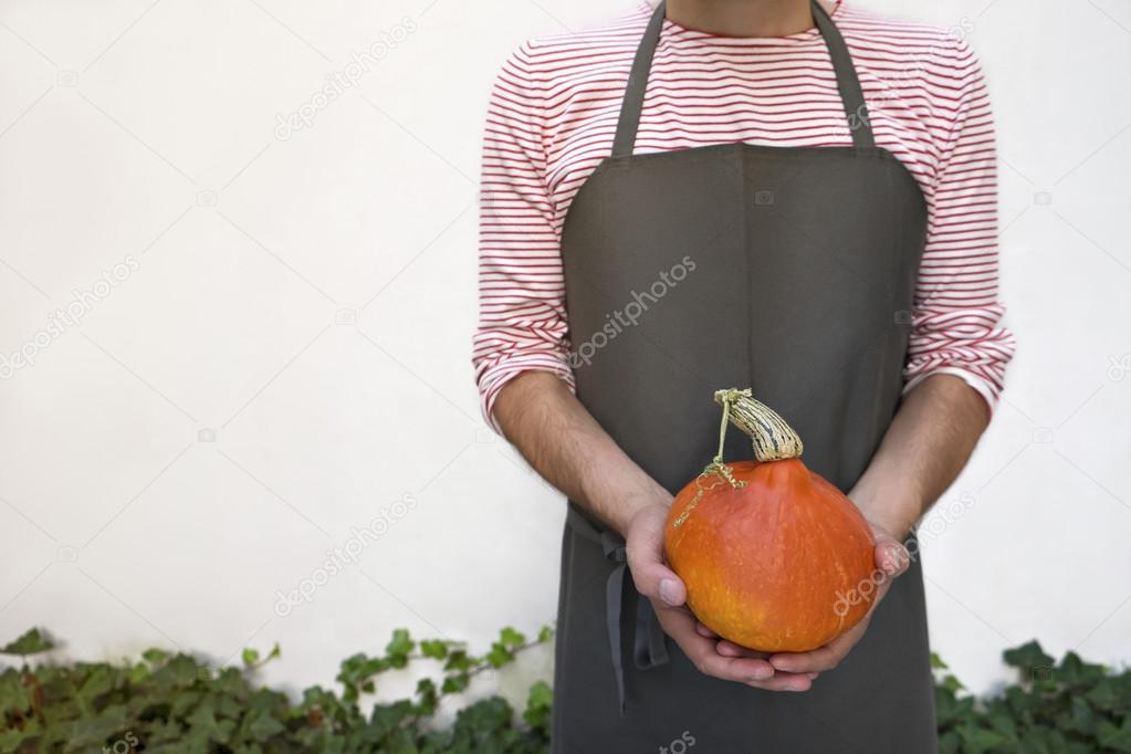 Farmer holding orange pumpkin.