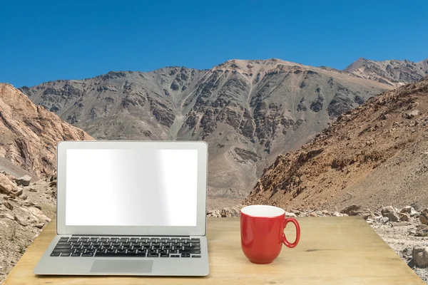 laptop and red mug on wood table with mountain in Leh ladakh, In