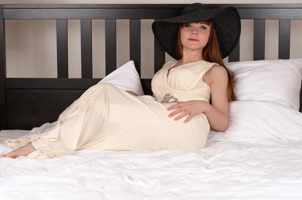 Mulher encantadora em um vestido e chapéu na cama — Fotografia de Stock