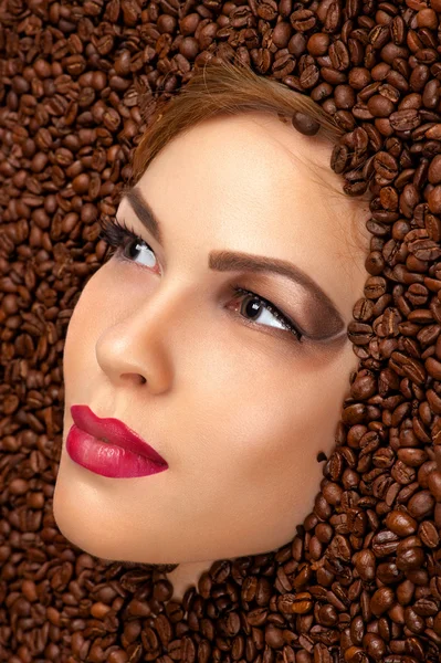 Mooie vrouw gezicht in koffiebonen — Stockfoto
