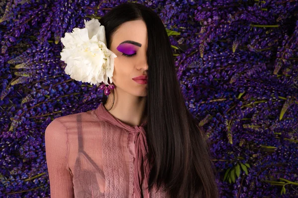 Bela mulher com peônia no cabelo no fundo flores lupinas — Fotografia de Stock