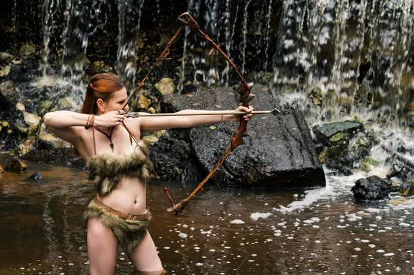 Mulher arqueiro brotos arco no fundo cachoeira — Fotografia de Stock