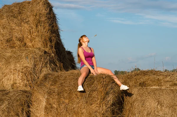 Attractive woman sitting on haystacks — Stock Photo, Image