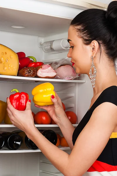 Beautiful woman chooses peppers from the fridge — Stock Photo, Image