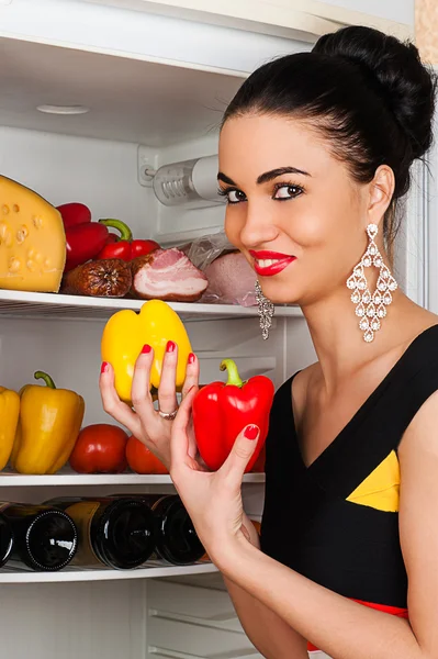 Beautiful woman takes peppers from the fridge smiling — Stock Photo, Image