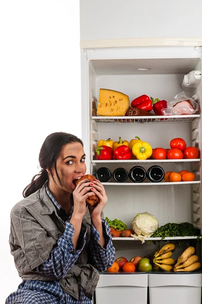 Голодная женщина ест мясо, сидя в холодильнике — стоковое фото