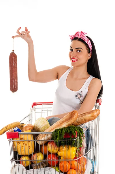 Woman sitting in a supermarket trolley with sausage in hand — Stock Photo, Image