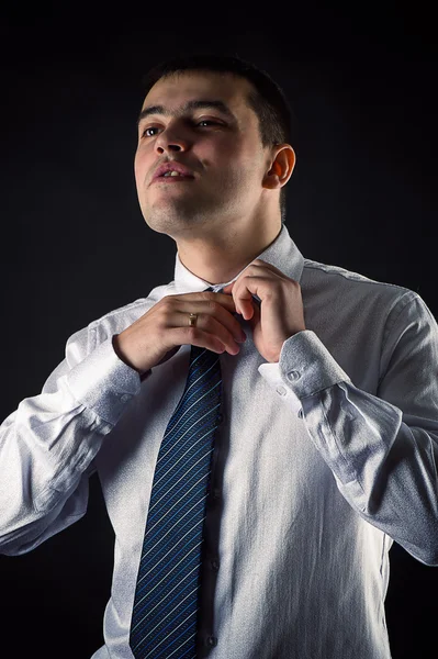 Handsome businessman corrects necktie isolated on black — Stock Photo, Image