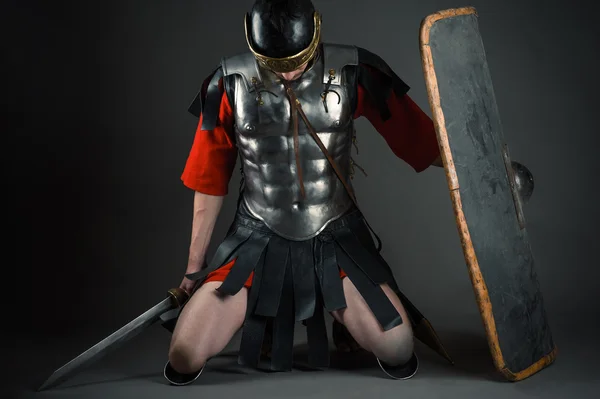 Tired soldier kneeling with a shield and a sword in hands — Stock Photo, Image