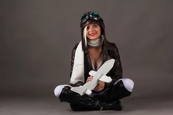 Улыбающаяся женщина в шляпе летчика сидит с игрушечным самолетом в руках — стоковое фото