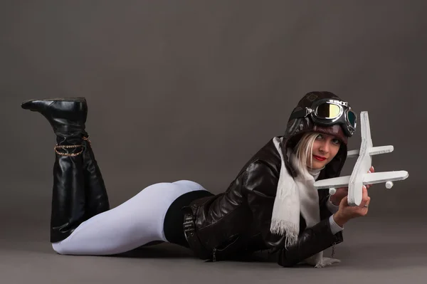 Sexy young woman in aviator hat lying on the floor with toy airplane in hands — 스톡 사진