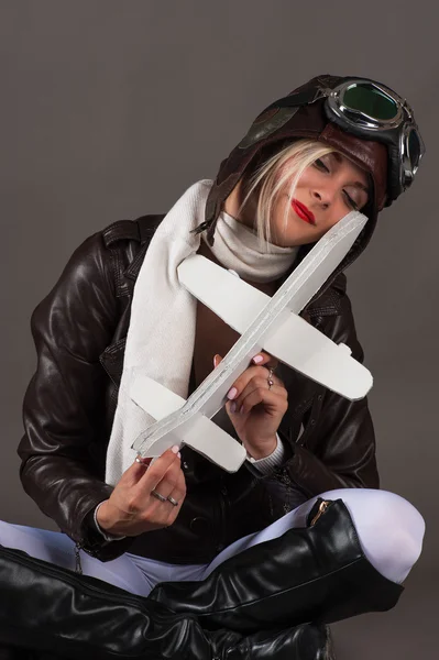 Frau mit Fliegermütze sitzt mit Spielzeugflugzeug in der Hand — Stockfoto