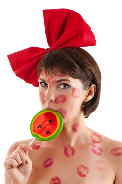 Hermosa chica con un lazo rojo y piruleta en la boca en lápiz labial besos —  Fotos de Stock