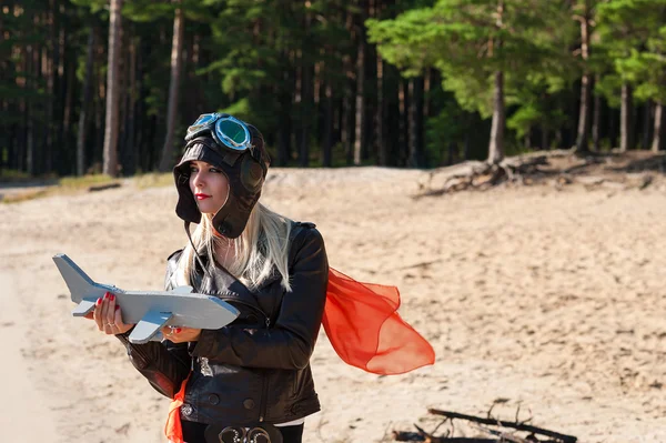 Drömmande kvinna i aviator hjälm på den på stranden med leksak flygplan — Stockfoto