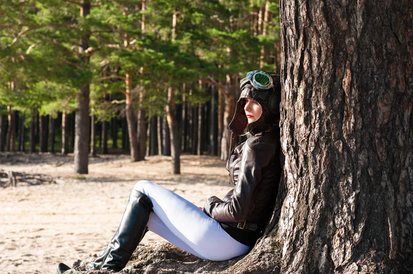 Einsame Frau im Helm des Piloten sitzt an einem Baum am Strand — Stockfoto